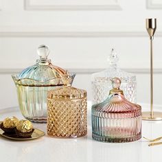 three glass jars sitting on top of a table next to gold spoons and a candle holder