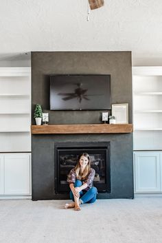 a woman sitting on the floor in front of a fireplace with a flat screen tv above it