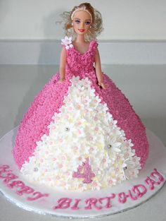 a birthday cake with a barbie doll on top and flowers all over the bottom,