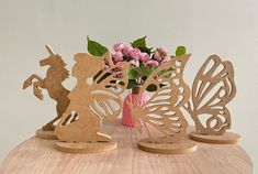 three wooden cut outs sitting on top of a table with pink flowers in vases