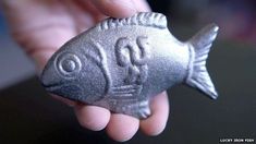 a hand holding a small silver fish figurine