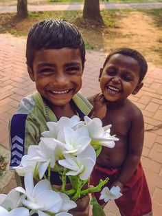 two young boys standing next to each other with flowers in front of their faces and smiling at the camera