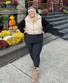 a woman is standing in front of some flowers wearing boots and a hat with her hands on her hips