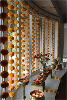 a long table filled with lots of food next to a wall covered in orange pom poms