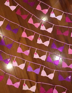 pink and purple bras are hanging from a string on a wooden floor with lights in the background