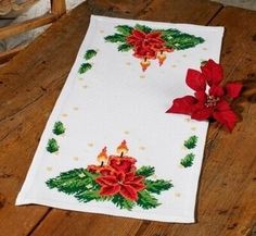 a white table cloth with poinsettis and holly on it sitting on a wooden floor