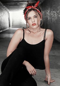 a woman sitting on the ground wearing black pants and a red bow in her hair