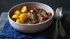 a bowl filled with meat and potatoes on top of a blue napkin next to a fork