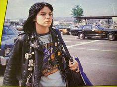 a woman in a leather jacket is walking down the street with her hand on her hip