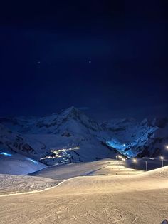 there is a snowboarder that is standing on the slope at night with mountains in the background