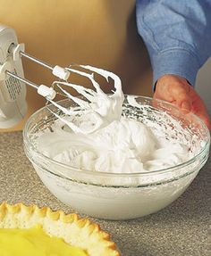 a person mixing whipped cream in a bowl next to a pie crust on the counter