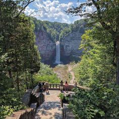 people are standing at the top of a cliff looking down on a waterfall in the distance