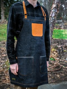 a man wearing an apron standing in front of a tree with his hands on his hips