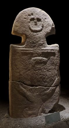 a large stone statue with a smiling face on it's head and arms, in a museum setting