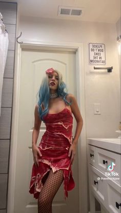 a woman with blue hair wearing a red dress and fishnet stockings in a bathroom