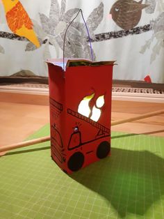 a red paper bag sitting on top of a green table next to a white curtain