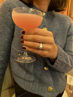 a woman is holding a pink drink in her hand and wearing a ring on her finger