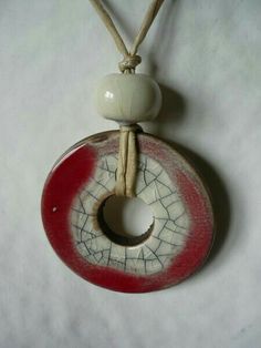 a red and white ceramic object hanging from a string on a white surface with a small hole in the middle