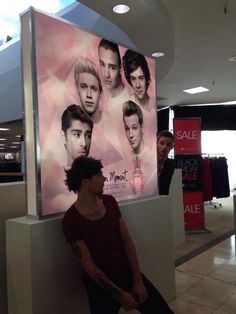 a man sitting on a counter in front of a large advertisement for men's hair products