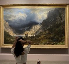 a woman looking at a painting in a museum with her hands up to the sky