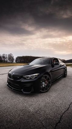 a black car is parked on the pavement in front of some trees and dark clouds