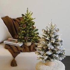 two small christmas trees sitting on top of a white couch next to a pillow and blanket