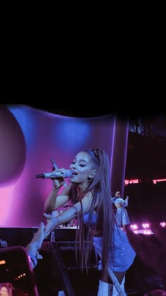 a woman with long hair on stage singing into a microphone and holding a cell phone in her hand