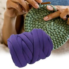 a woman is holding a green purse with purple yarn on it and knitting the handle