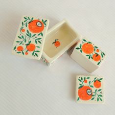 three small boxes with oranges painted on them sitting on a white tableclothed surface