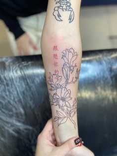 a woman with a tattoo on her arm holding up a flower and chinese writing in front of her arm