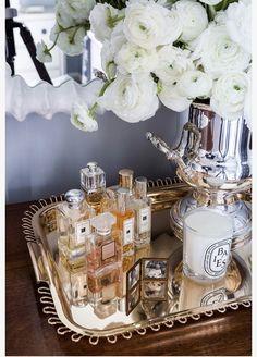 a tray with perfumes and flowers on it next to a vase filled with white roses