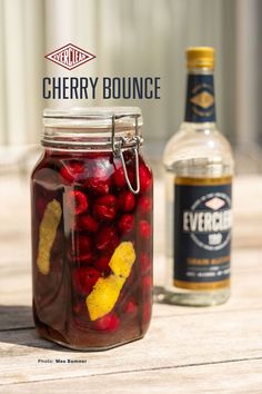 a jar filled with cherries next to a bottle of alcohol