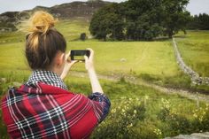 a woman taking a photo with her cell phone in a field near a country road