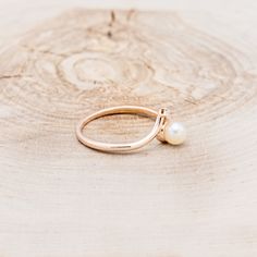 a gold ring with a pearl on it sitting on top of a piece of wood