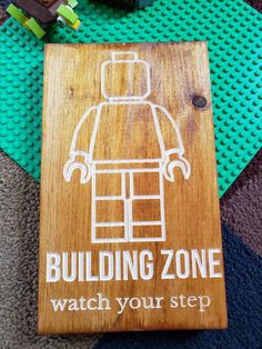 a wooden sign that says, building zone watch your step on the floor next to legos