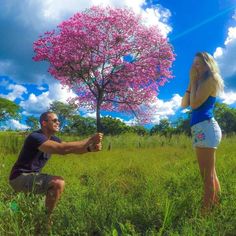 a man kneeling down next to a woman in a field under a pink flowered tree