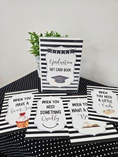 four graduation cards sitting on top of a black and white tablecloth with cupcakes