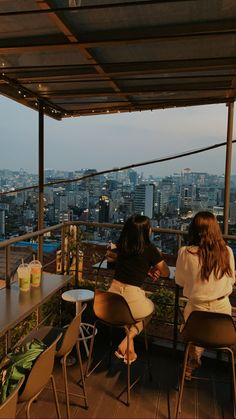 two women sitting at a table on top of a building with city in the background