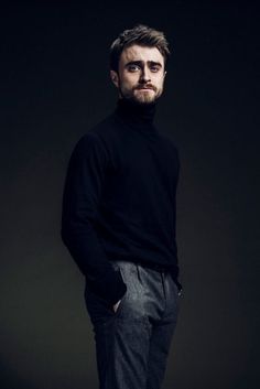 a man standing with his hands in his pockets and wearing a black turtle neck sweater