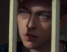 a close up of a person behind bars looking at the camera with blue eyes and red hair