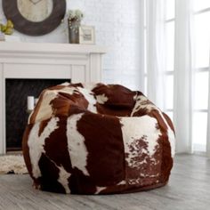 a brown and white cow print bean bag sitting on top of a wooden floor next to a fireplace