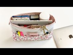 an open purse sitting on top of a white table next to a laptop computer and cell phone