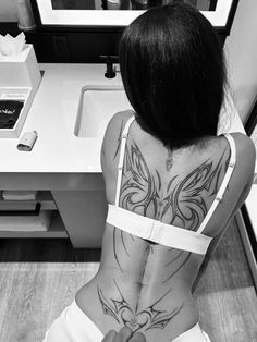 a woman with a tattoo on her back sitting in front of a sink and mirror