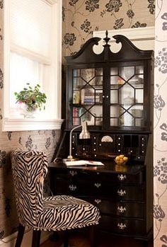 a zebra print chair sits in front of a desk with a black hutch and china cabinet