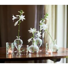 several vases with flowers in them sitting on a table next to glasses and candles