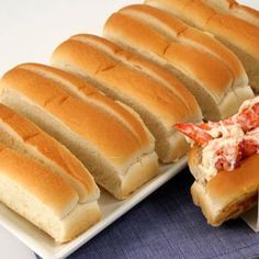 two plates with lobster sandwiches on them next to a blue napkin and white plate full of lobsters