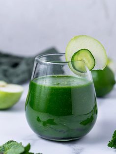 a glass filled with green liquid next to sliced cucumbers