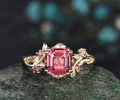 a pink tourmaline ring sitting on top of a green rock with leaves around it