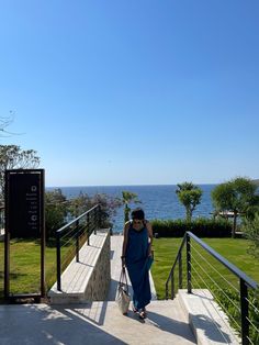 a woman is walking up some stairs towards the ocean with her hand in her pocket