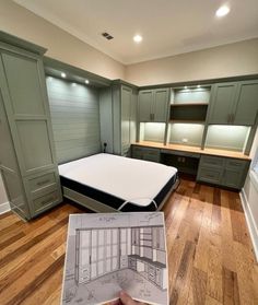 a person holding up a drawing in front of a room with green cabinets and drawers